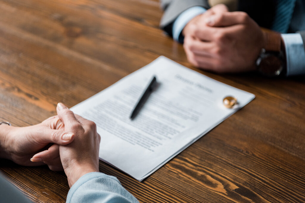 partial view of lawyer and client sitting at table with divorce decree and wedding rings