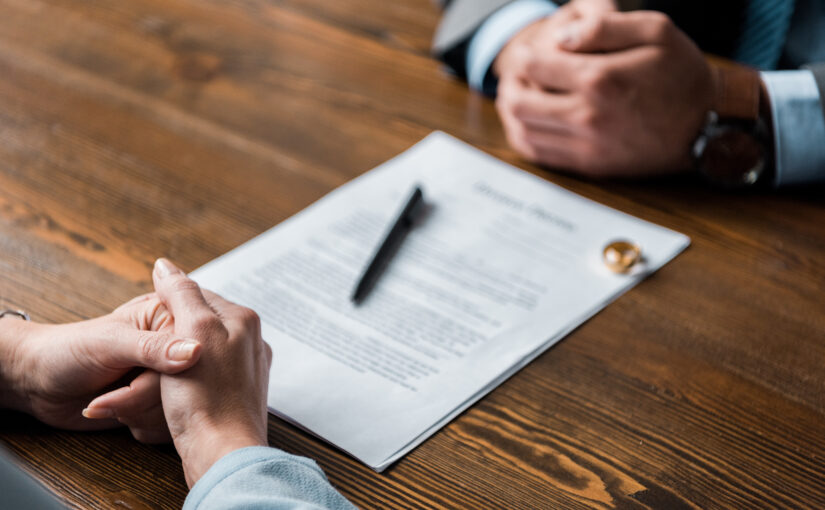 partial view of lawyer and client sitting at table with divorce decree and wedding rings